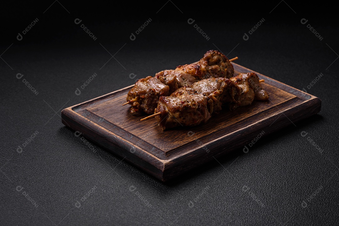 Delicioso espetinho frito de frango ou carne de porco com sal, especiarias e ervas sobre um fundo escuro de concreto