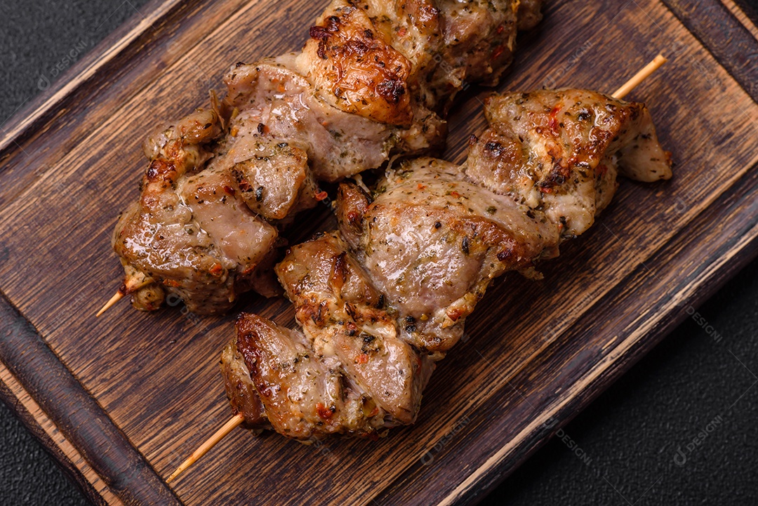 Delicioso espetinho frito de frango ou carne de porco com sal, especiarias e ervas sobre um fundo escuro de concreto