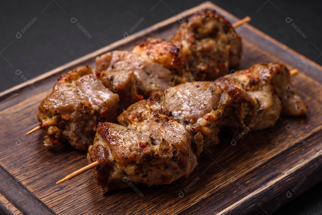 Delicioso espetinho frito de frango ou carne de porco com sal, especiarias e ervas sobre um fundo escuro de concreto