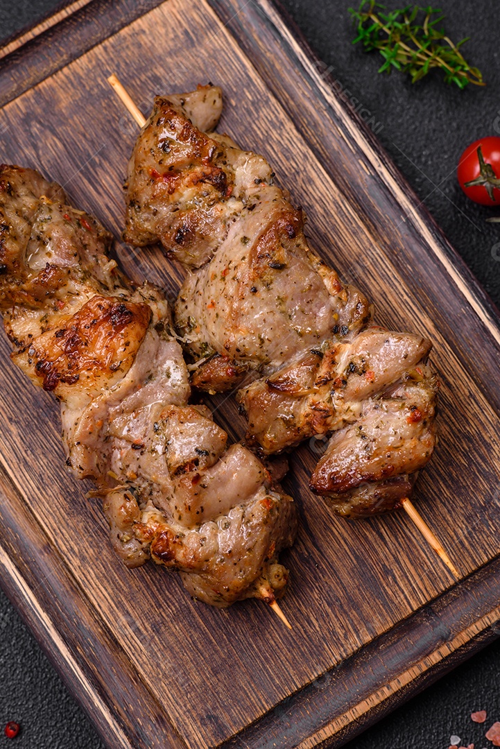 Delicioso espetinho frito de frango ou carne de porco com sal, especiarias e ervas sobre um fundo escuro de concreto