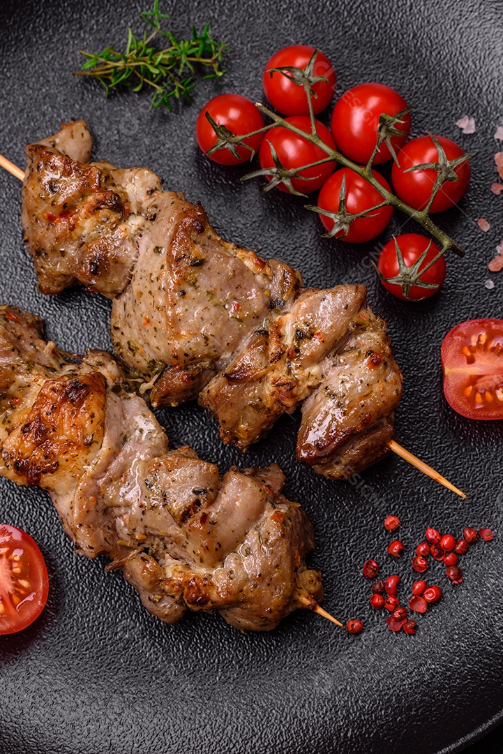 Delicioso espetinho frito de frango ou carne de porco com sal, especiarias e ervas sobre um fundo escuro de concreto