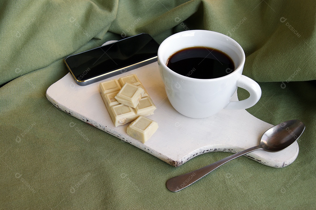 Celular e xícara de café com chocolates e colher e em cima de tábua