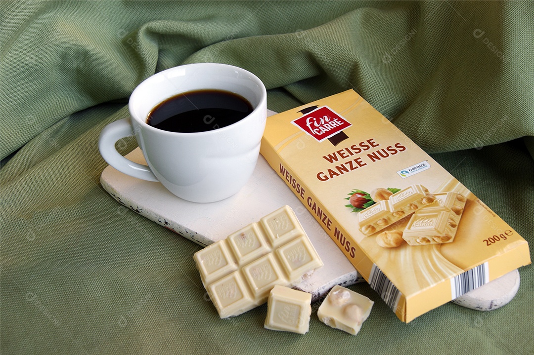 Xícara com café e barras de chocolate ao lado em cima de tábua sobre pano verde