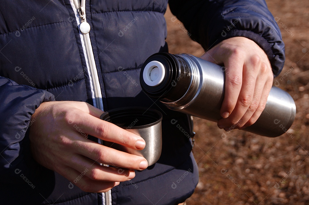 Mãos do homem derramando chocolate quente fresco da garrafa térmica para a xícara