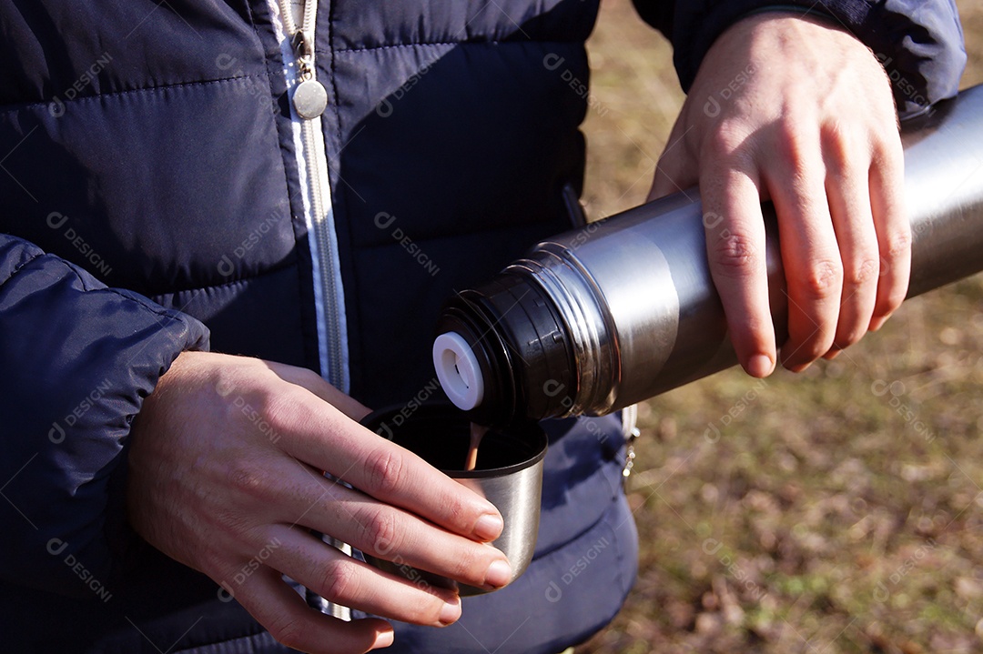 Mãos do homem derramando chocolate quente fresco da garrafa térmica para a xícara