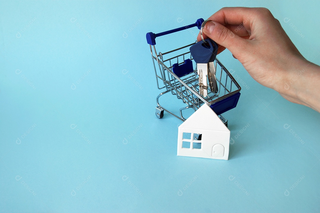 Carrinho de compra casa de papel e mão segurando chave sobre fundo azul