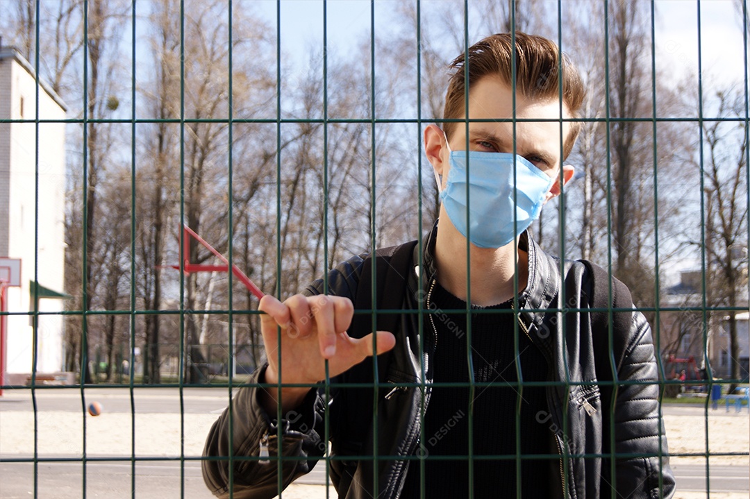 Homem de máscara atras de grade de ferro segurando