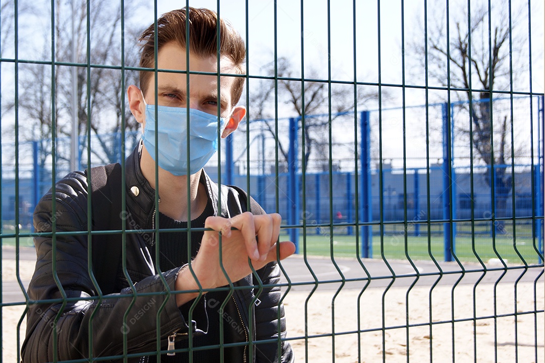 Homem de máscara com mão na grade de um cercado