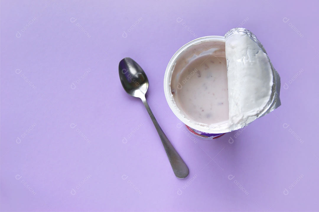 Iogurte de morango no copo plástico e colher ao lado sobre fundo roxo