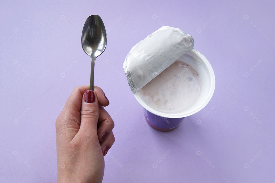 Iogurte de morango com pedaços dentro de um copo plástico e mão segurando colher