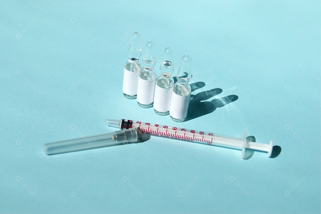 Seringa com agulha e várias ampolas de remédio sobre fundo azul