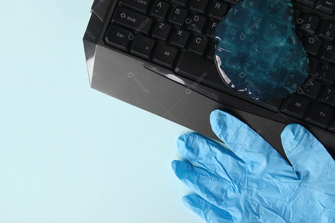 Teclado com gel de limpeza em cima e luva ao lado