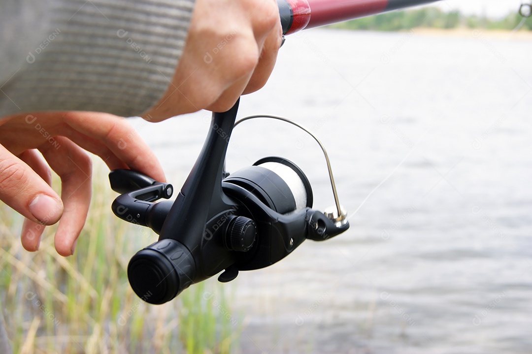Mãos segurando vara de pescar sobre rio