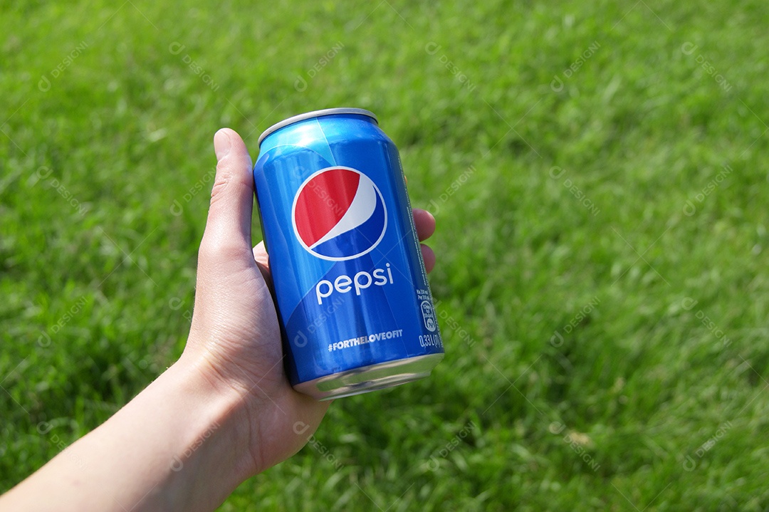 Mão segurando refrigerante Pepsi em fundo gramado