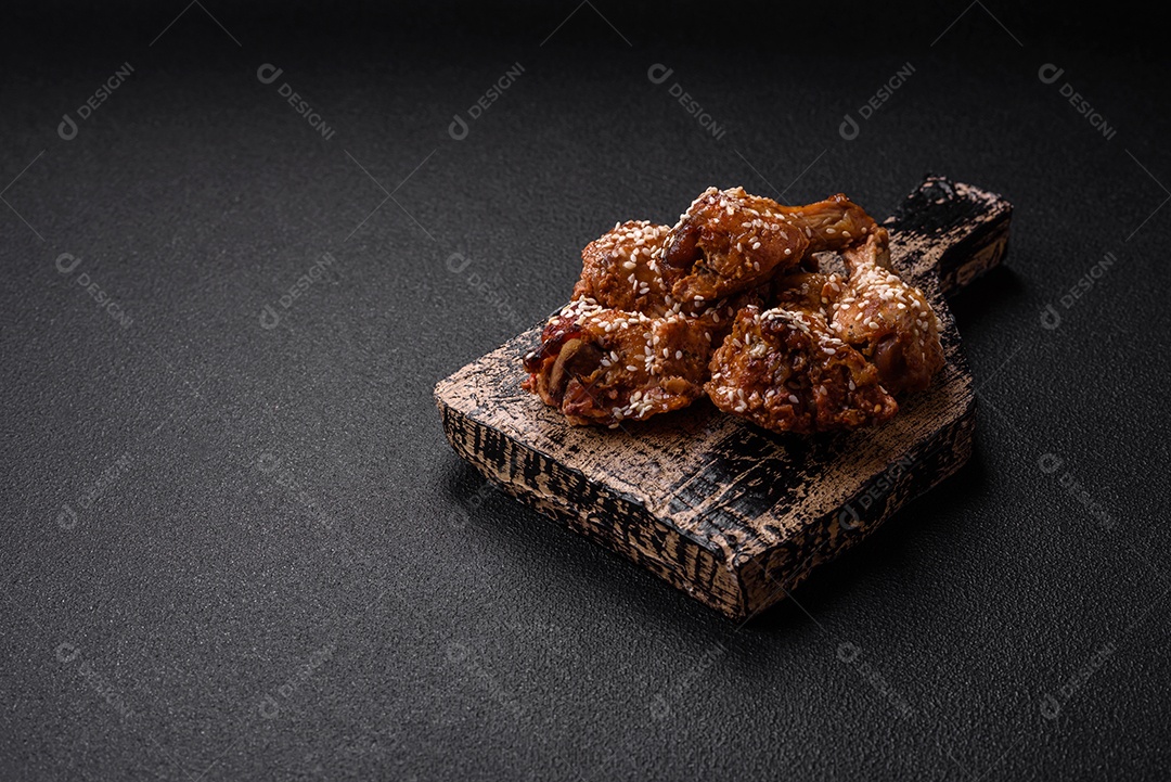 Deliciosas asas de frango grelhado com sal, especiarias e molho teriyaki sobre um fundo escuro de concreto