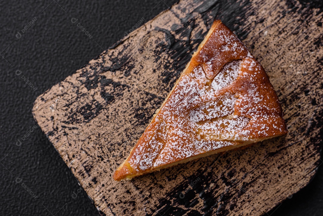 Um pedaço de torta caseira assada com maçã ou pêra, com canela, polvilhada com pó sobre um fundo escuro de concreto