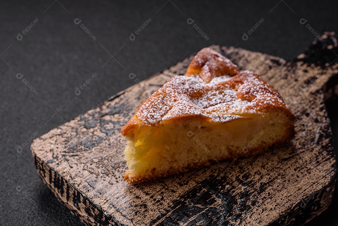 Um pedaço de torta caseira assada com maçã ou pêra, com canela, polvilhada com pó sobre um fundo escuro de concreto