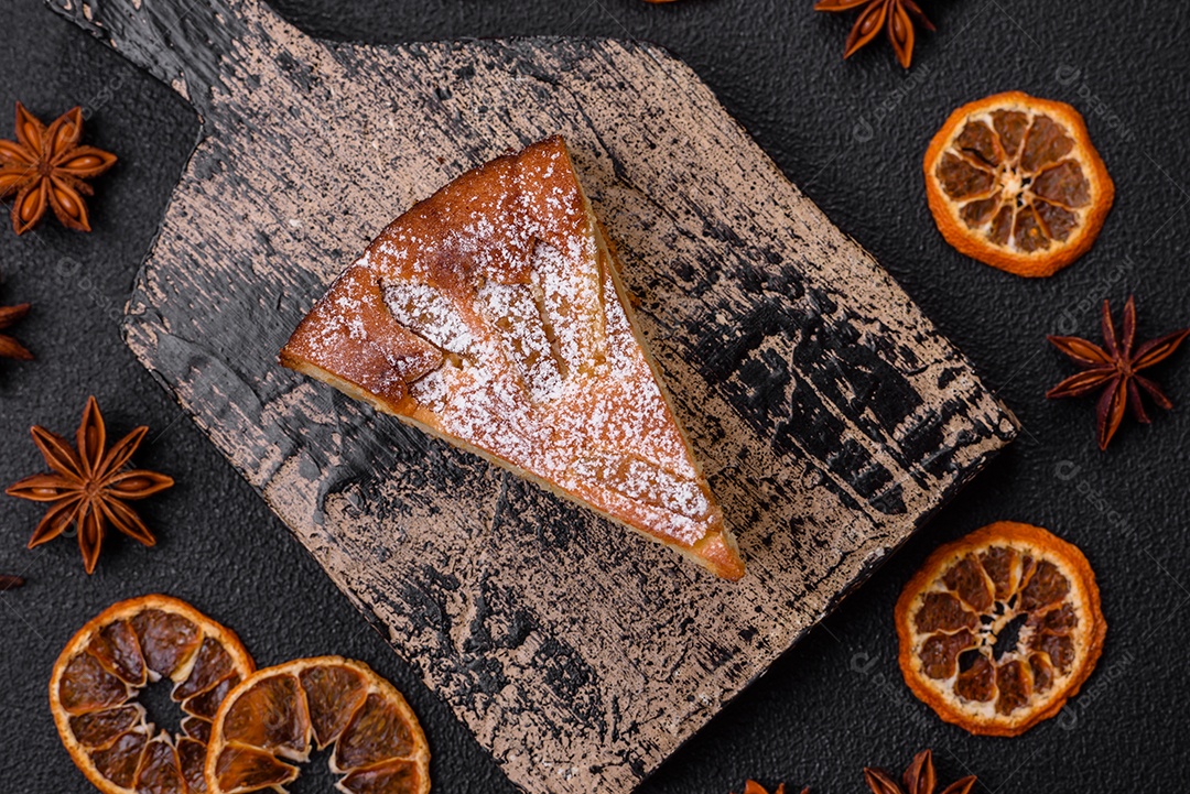 Um pedaço de torta caseira assada com maçã ou pêra, com canela, polvilhada com pó sobre um fundo escuro de concreto