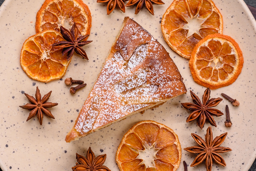 Um pedaço de torta caseira assada com maçã ou pêra, com canela, polvilhada com pó sobre um fundo escuro de concreto