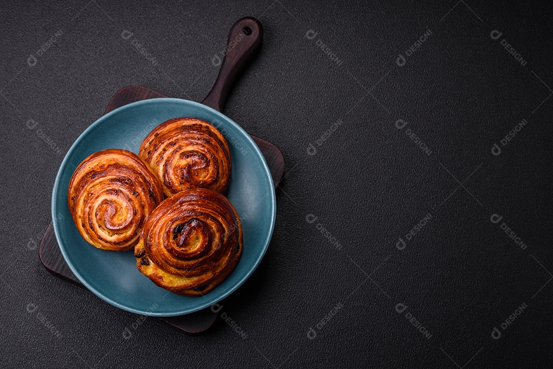 Deliciosos rolos de passas de canela assados ​​em forma de rolos sobre um fundo escuro de concreto