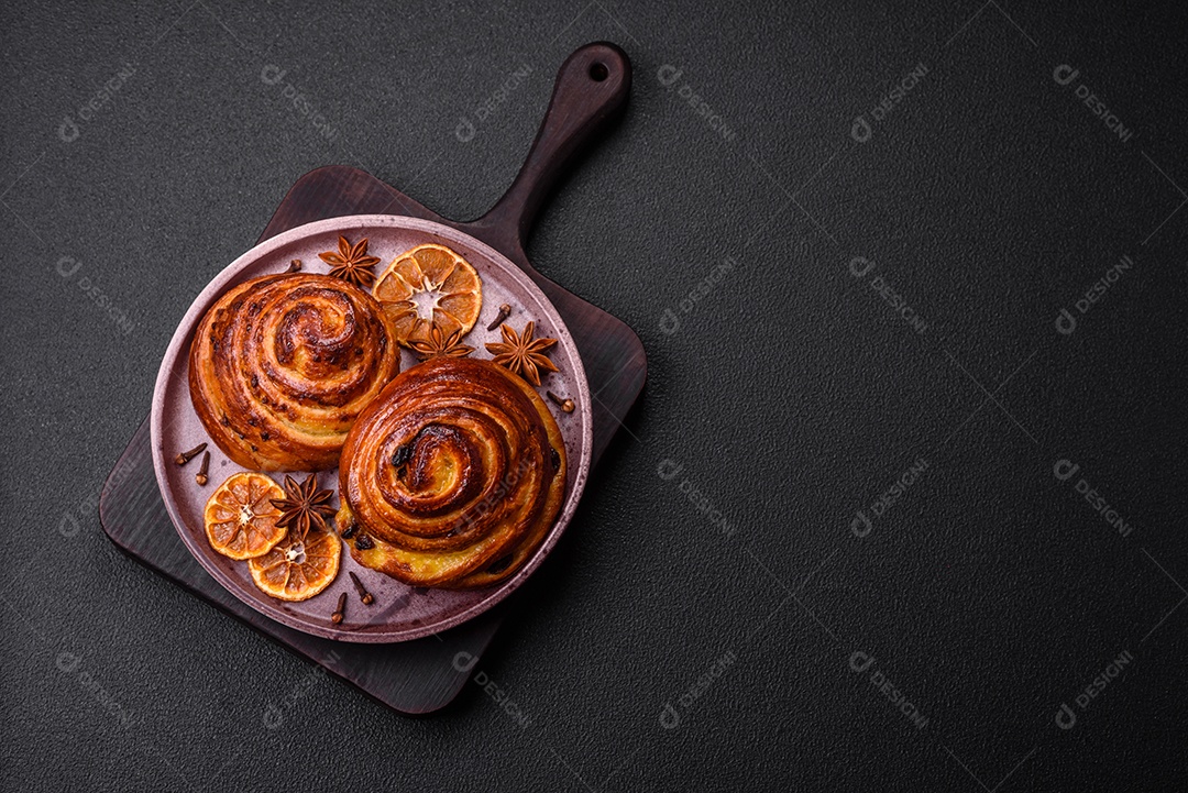 Deliciosos rolos de passas de canela assados ​​em forma de rolos sobre um fundo escuro de concreto