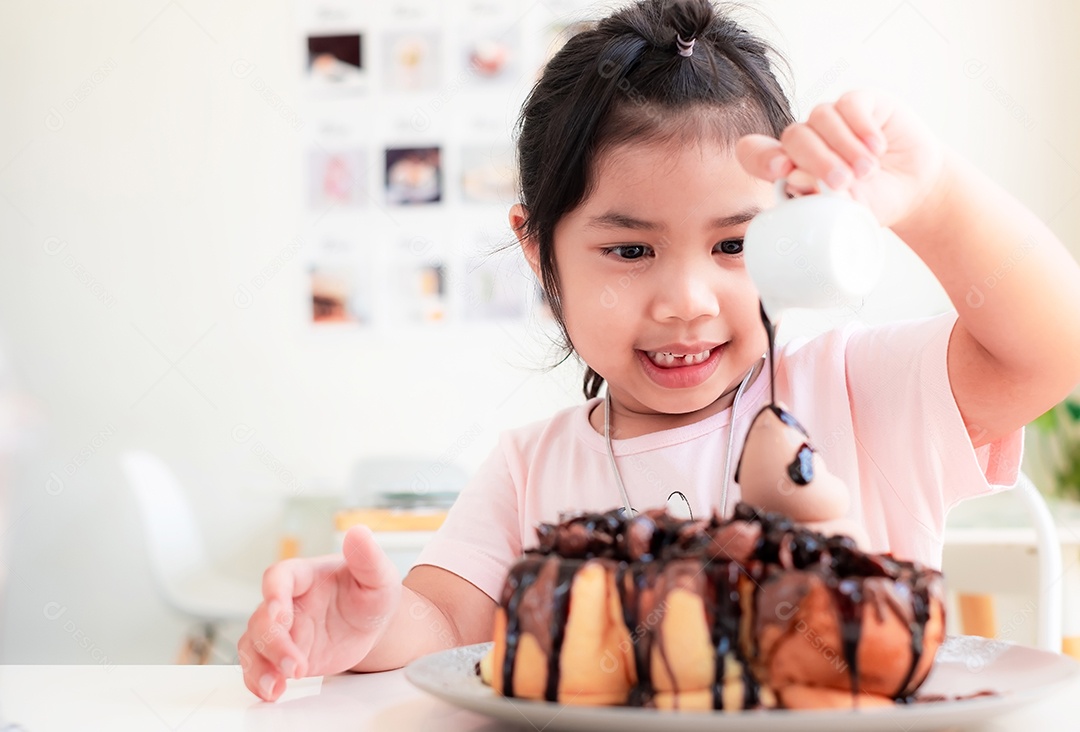 Linda menina asiática está sorrindo e derramando chocolate em bolo