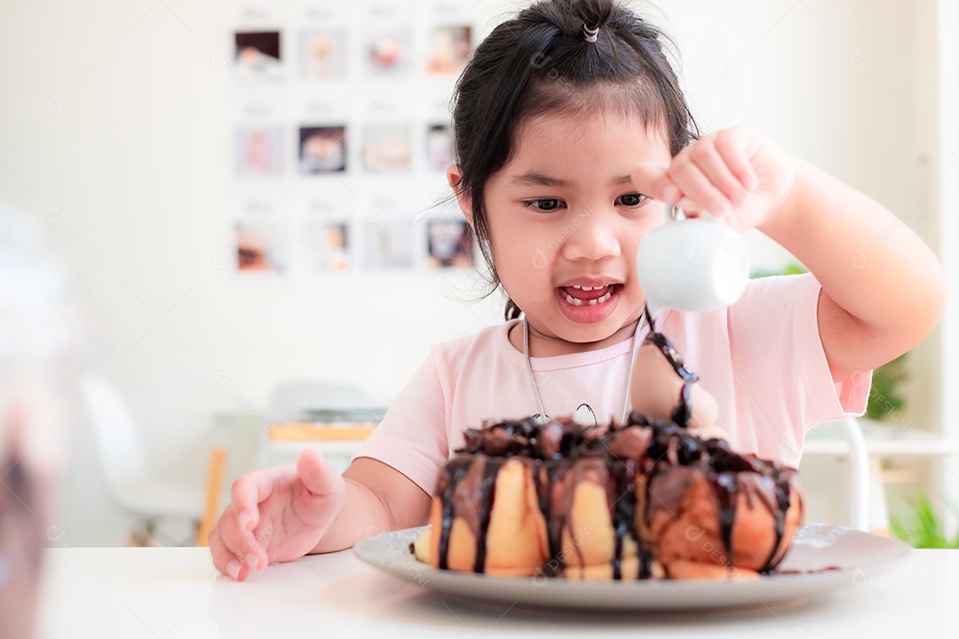 Linda menina asiática está sorrindo e derramando chocolate em bolo