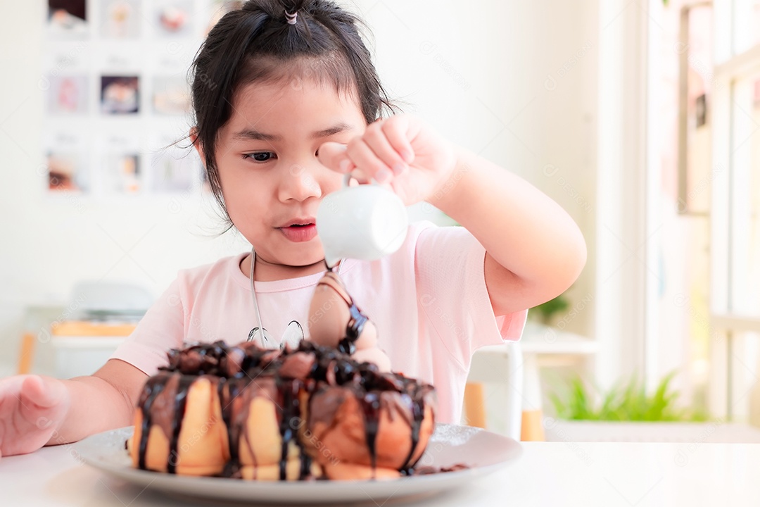 Linda menina asiática está sorrindo e derramando chocolate em bolo