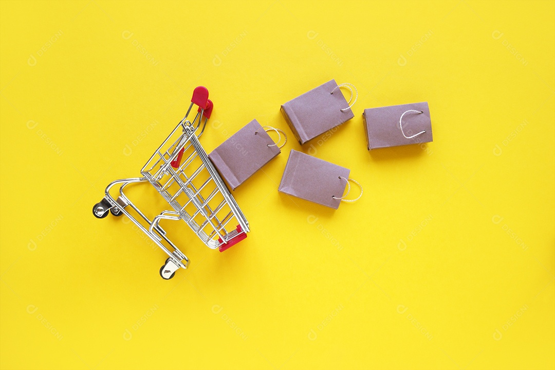 Sacolas kraft caídas junto ao carrinho de compra sobre fundo amaelo