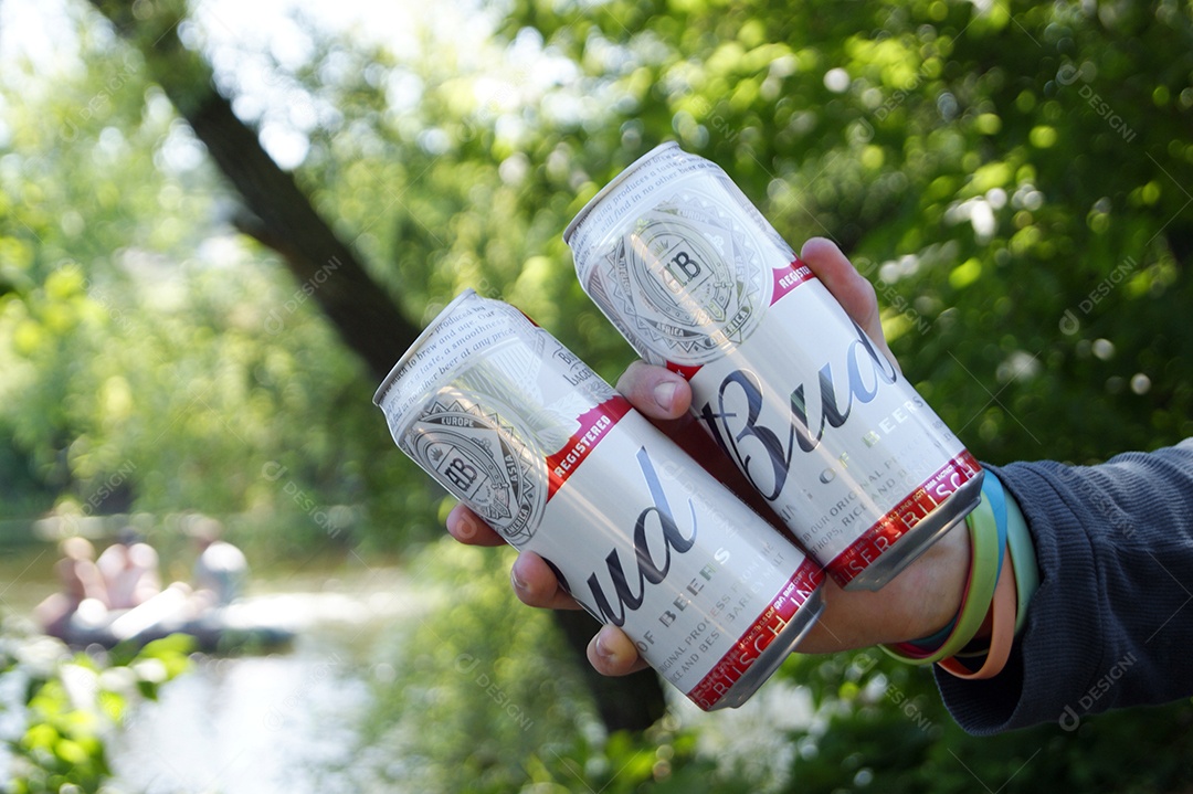 Mãos segurando duas latas de cervejas sobre fundo de natureza