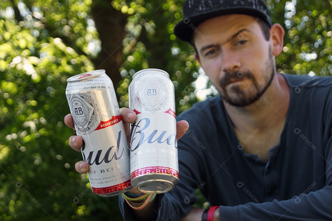Homem com duas latas de cervejas na mão sobree fundo de natureza