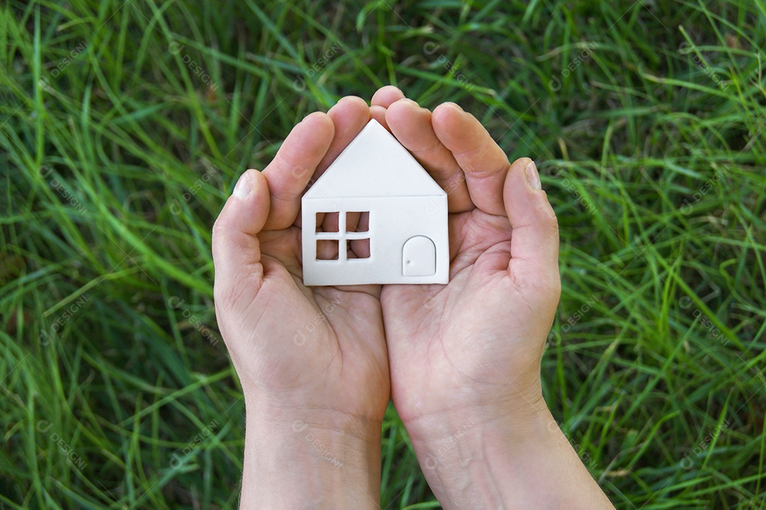 Mãos segurando casinha de papel sobre fundo gramado verde