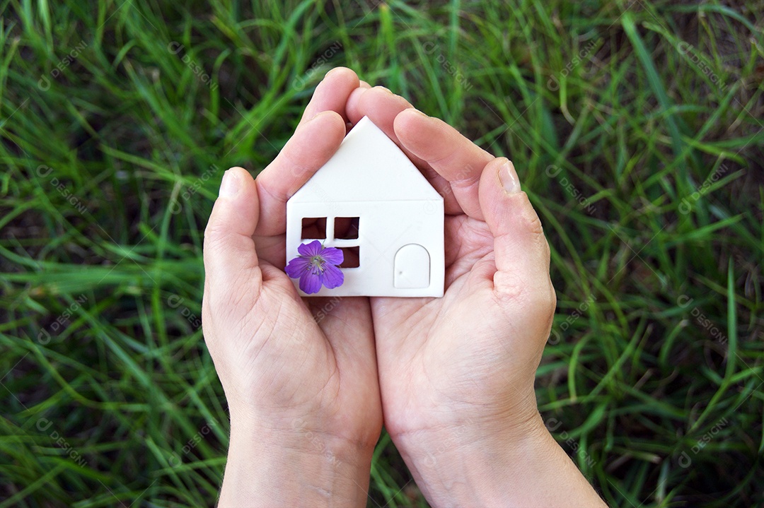 Mãos segurando mini casa branca sobre fundo grama verde