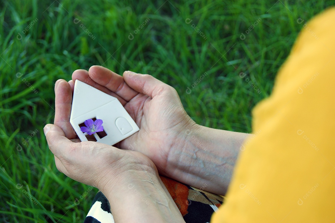 Mãos segurando casa sobre fundo de um terreno verde
