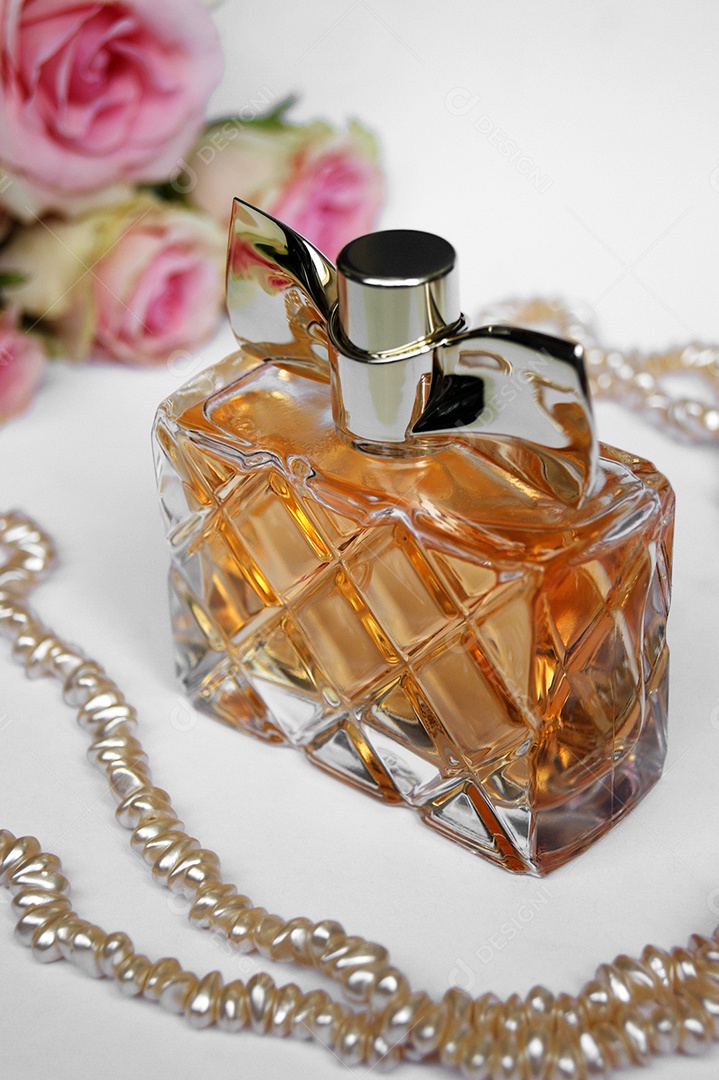 Frasco de perfume com flores ao lado e pérolas