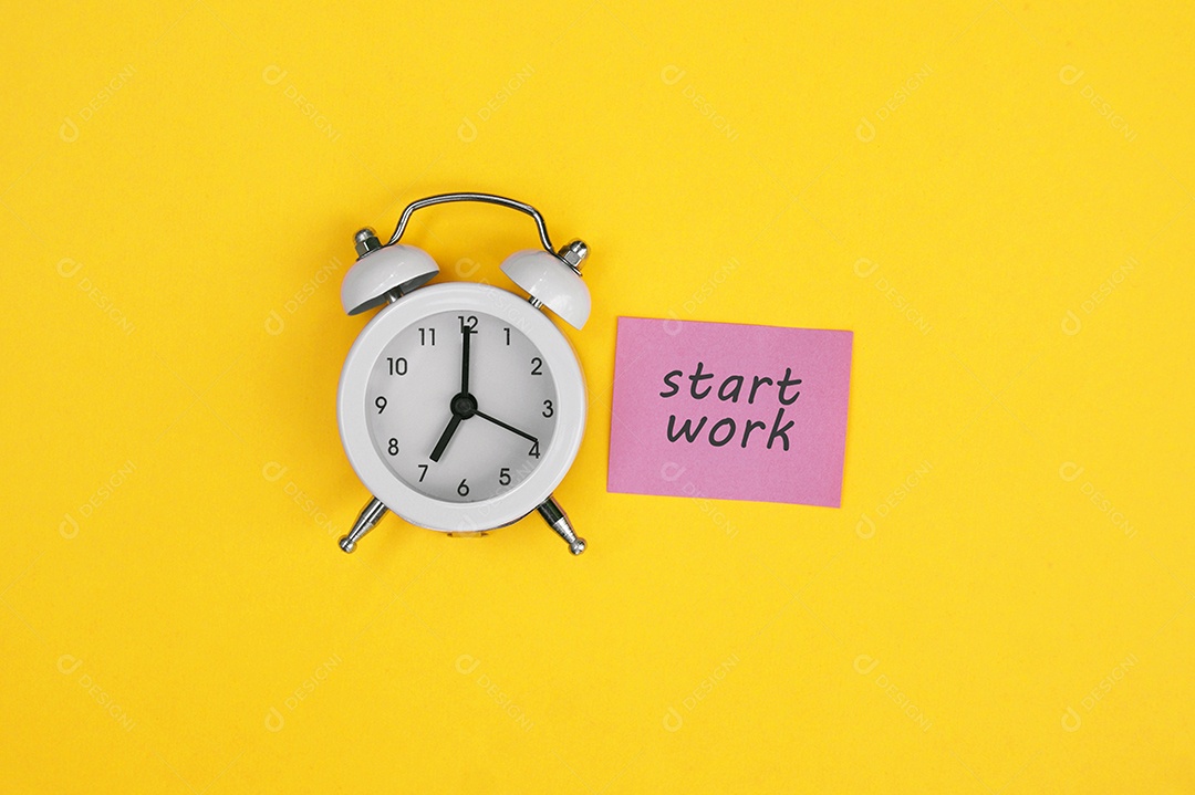 Despertador vintage branco e um adesivo escrito Começar a trabalhar em fundo amarelo