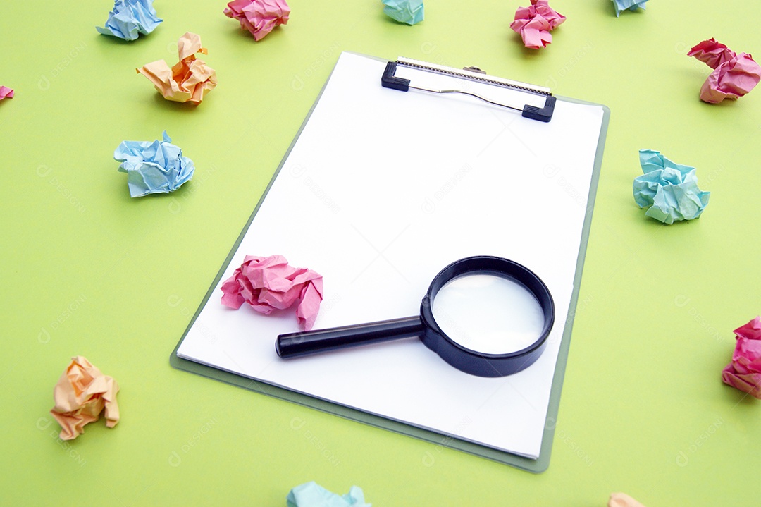 Papéis colorido amassados ao redor de prancheta com lupa