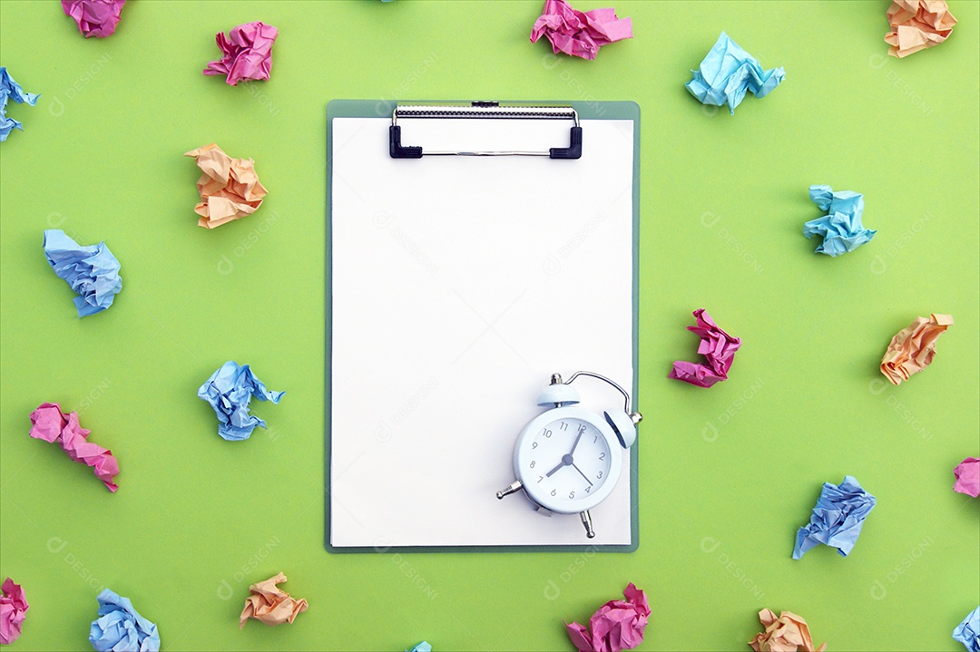 Papéis coloridos amassados ao redor de prancheta com relógio em cima
