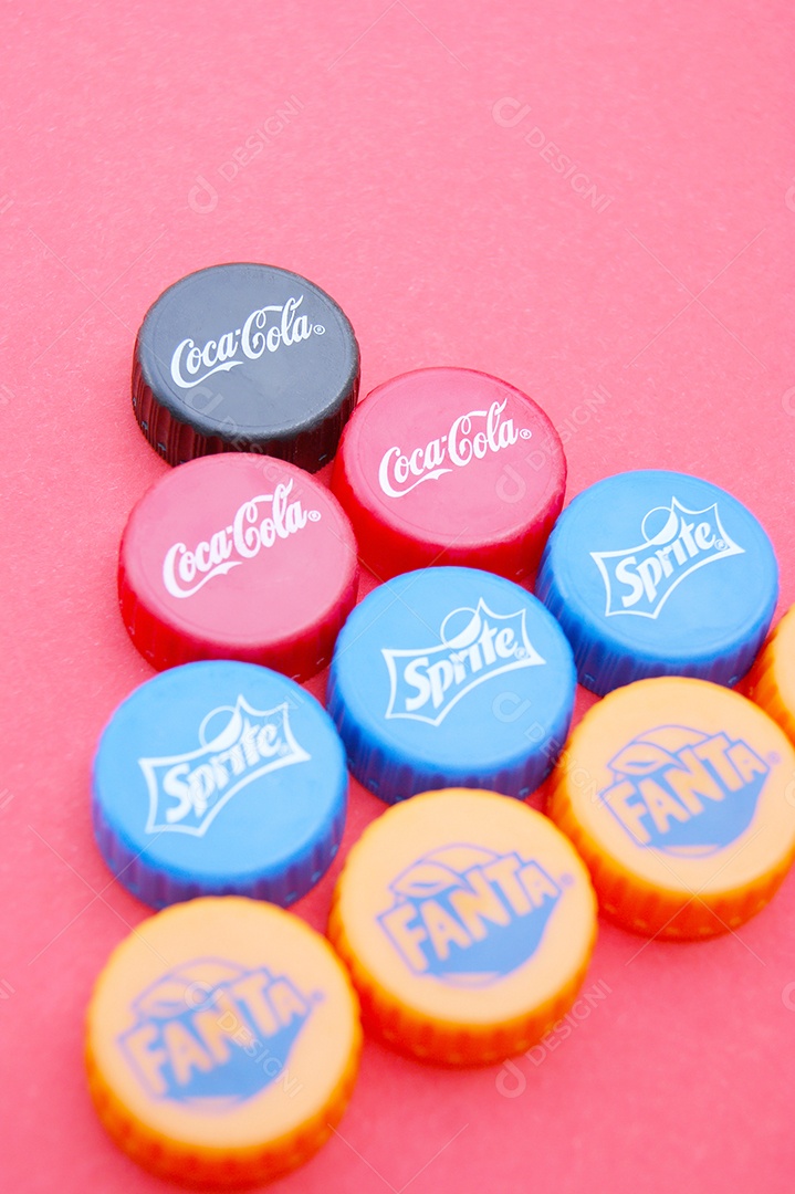 Várias tampas de garrafa pet de diferentes refrigerantes sobre fundo rosa