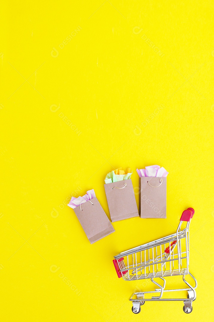 Carrinho de compra e sacolas sobre fundo amarelo