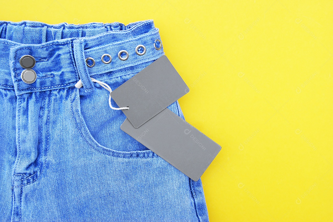 Roupa jeans com etiquetas sobre fundo amarelo