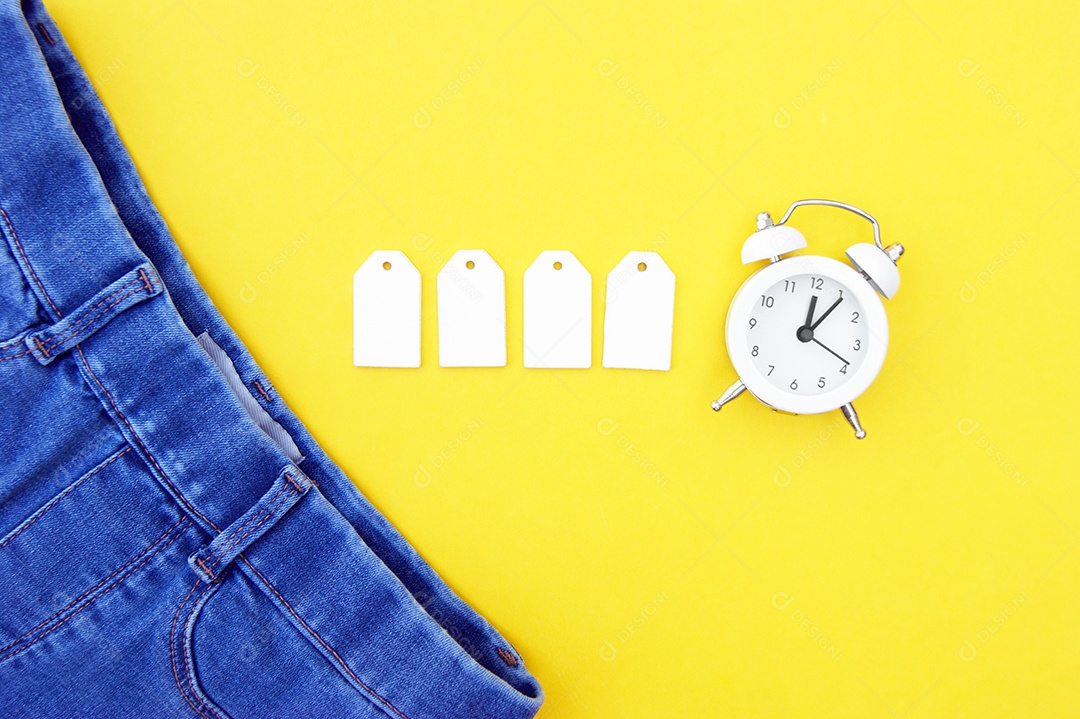 Jeans com quatro etiqueta em branco e relógio sobre fundo amarelo