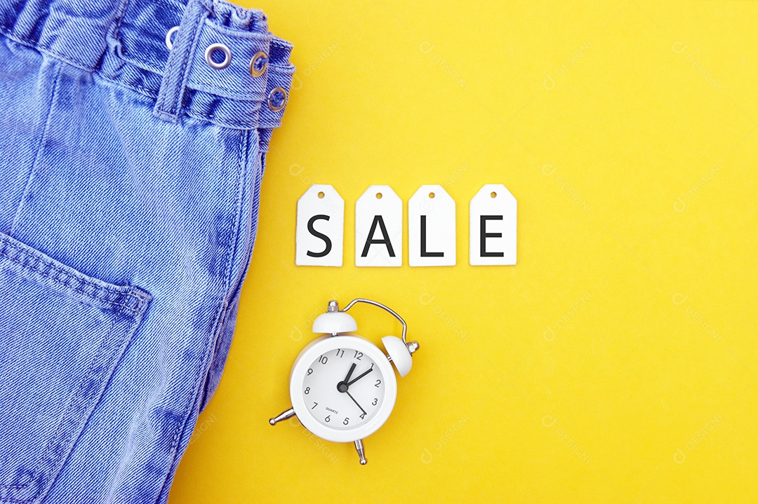Roupa jeans com etiquetas com palavra Venda e relógio sobre fundo amarelo