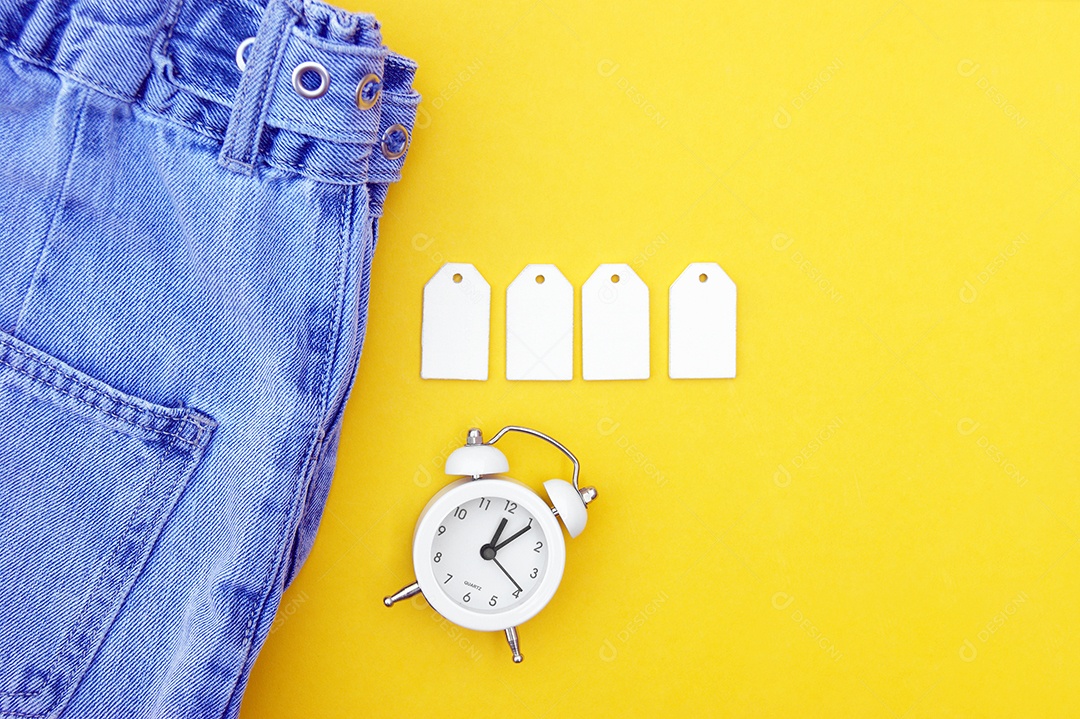Roupa jeans com etiquetas e relógio sobre fundo amarelo