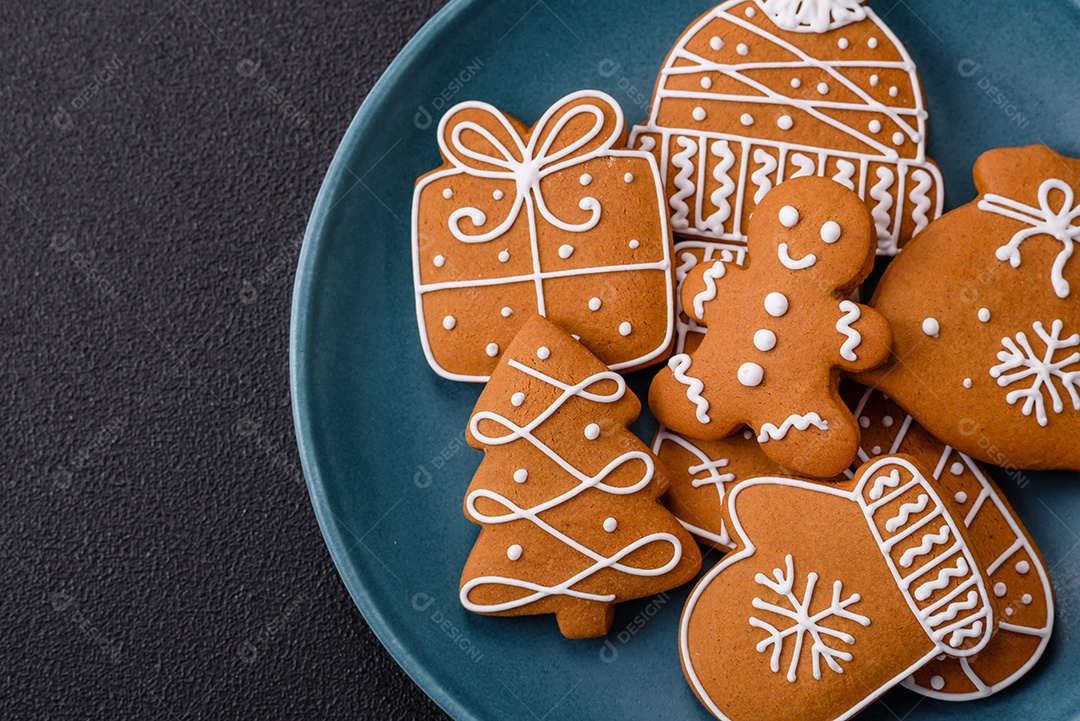 Lindos biscoitos de gengibre de Natal de cores diferentes em uma placa de cerâmica sobre uma mesa de concreto escuro
