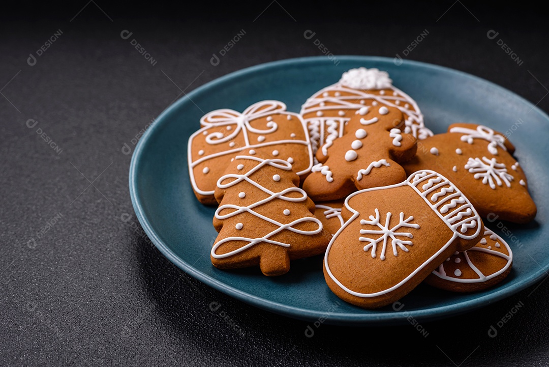 Lindos biscoitos de gengibre de Natal de cores diferentes em uma placa de cerâmica sobre uma mesa de concreto escuro