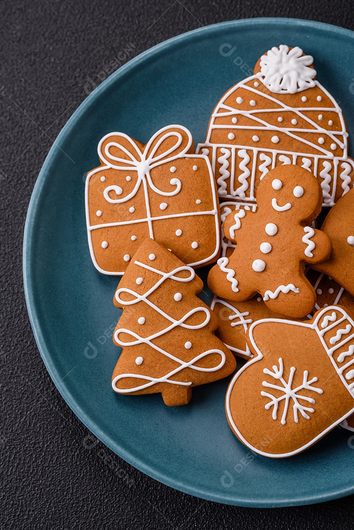 Lindos biscoitos de gengibre de Natal de cores diferentes em uma placa de cerâmica sobre uma mesa de concreto escuro