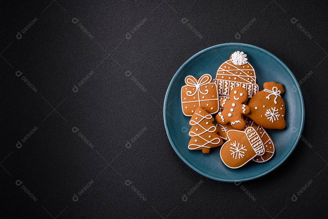 Lindos biscoitos de gengibre de Natal de cores diferentes em uma placa de cerâmica sobre uma mesa de concreto escuro