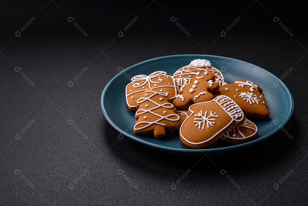 Lindos biscoitos de gengibre de Natal de cores diferentes em uma placa de cerâmica sobre uma mesa de concreto escuro