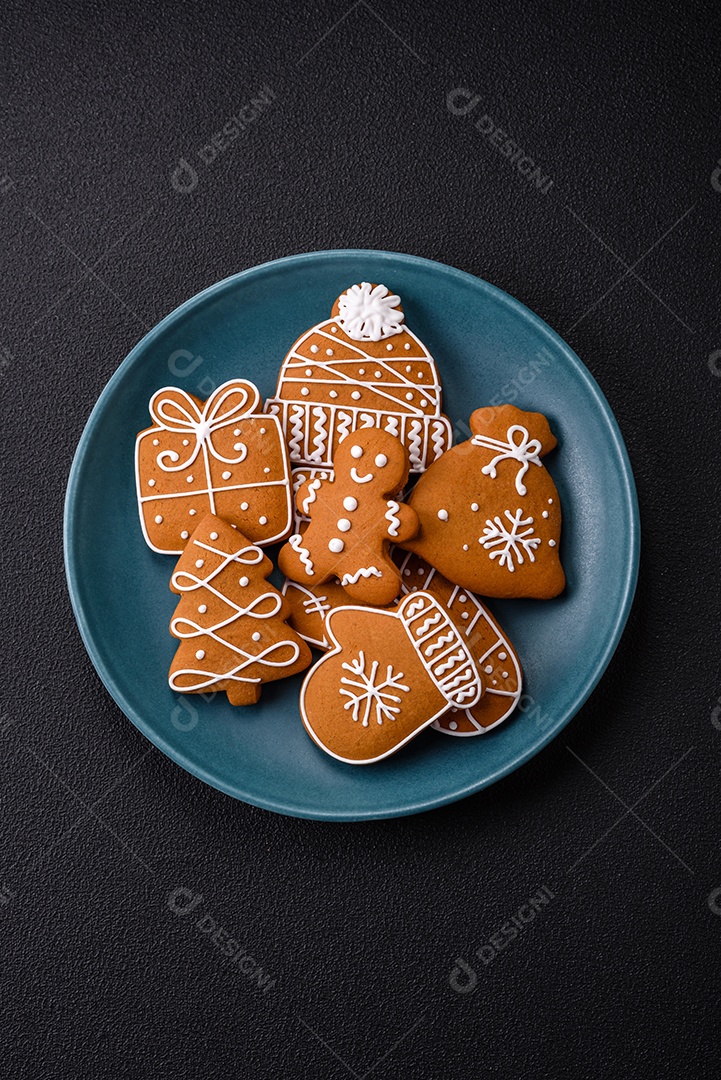 Lindos biscoitos de gengibre de Natal de cores diferentes em uma placa de cerâmica sobre uma mesa de concreto escuro